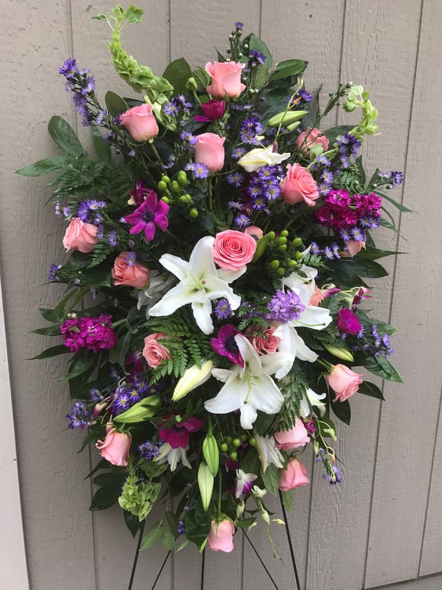 Sympathy standing spray of white lilies, pink roses, and purple accents