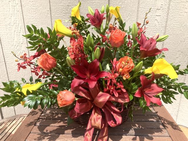 Fireside basket of red, orange, and yellow flowers with a jewel-tone ribbon