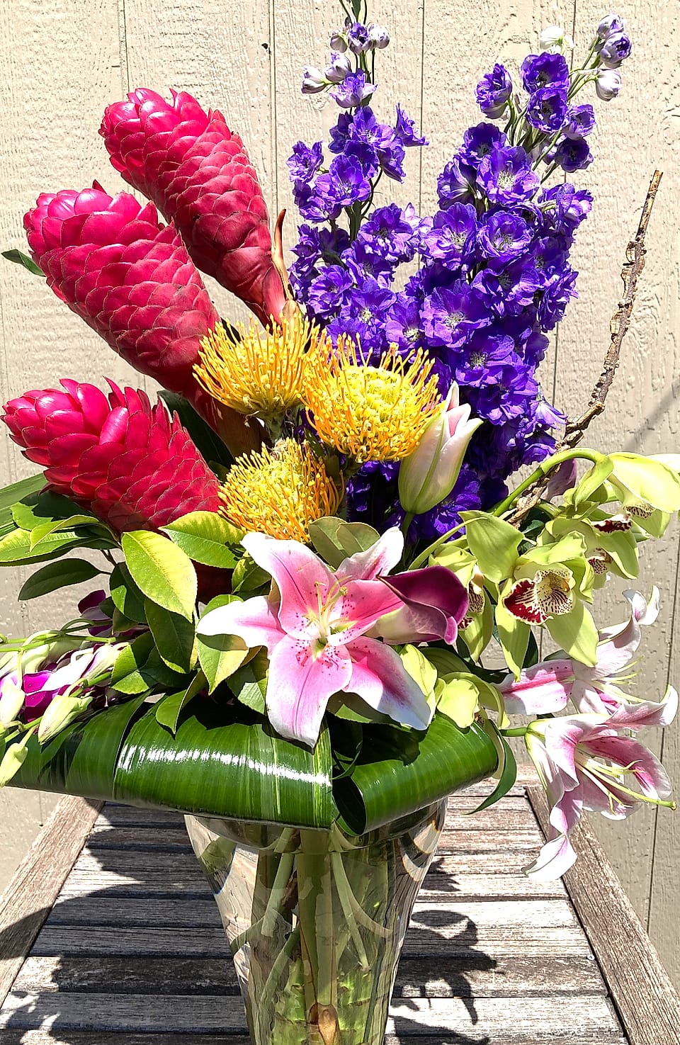 Tall arrangement of pink ginger, purple delphinium, pincushion protea, and stargazer lilies