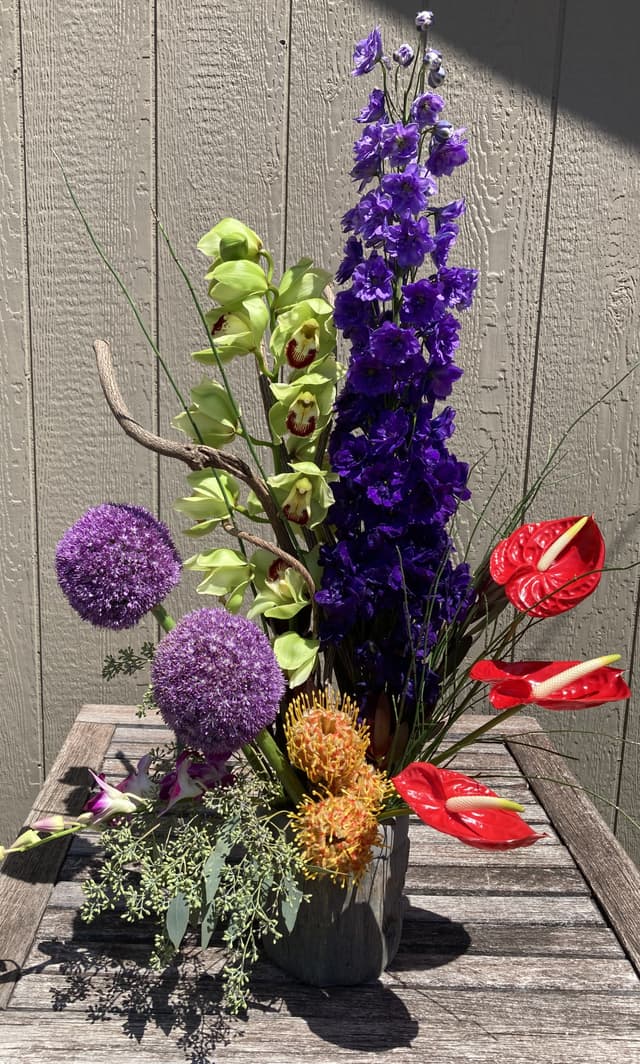Vertical arrangement of purple delphinium, allium, red anthurium, and pincushion protea