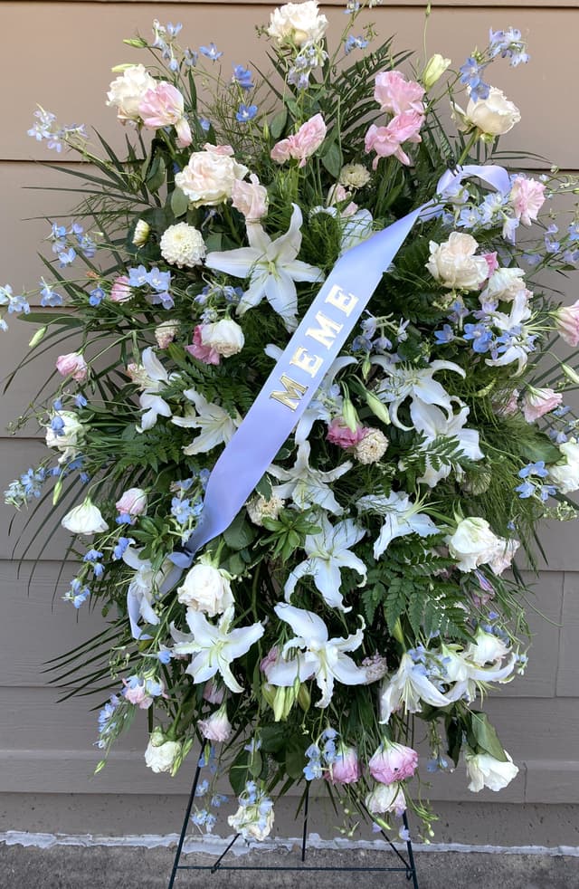 Standing easel spray of white lilies and roses with a pale blue ribbon