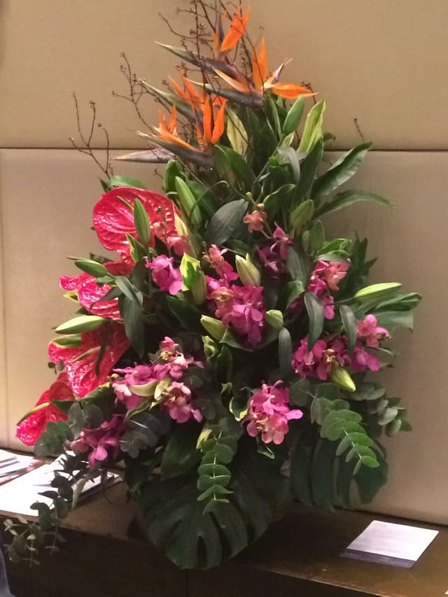 Sympathy spray of pink orchids, roses, and tropical foliage