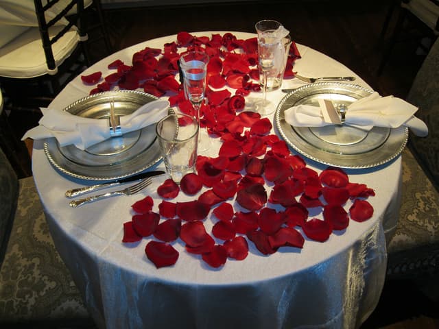 Sweetheart table scattered with red rose petals and champagne glasses