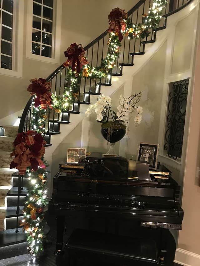 Staircase dressed with Christmas garland and floral accents by a grand piano
