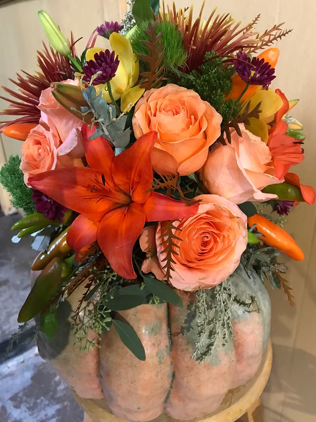 Fall arrangement of orange roses, lilies, and berries designed in a pumpkin